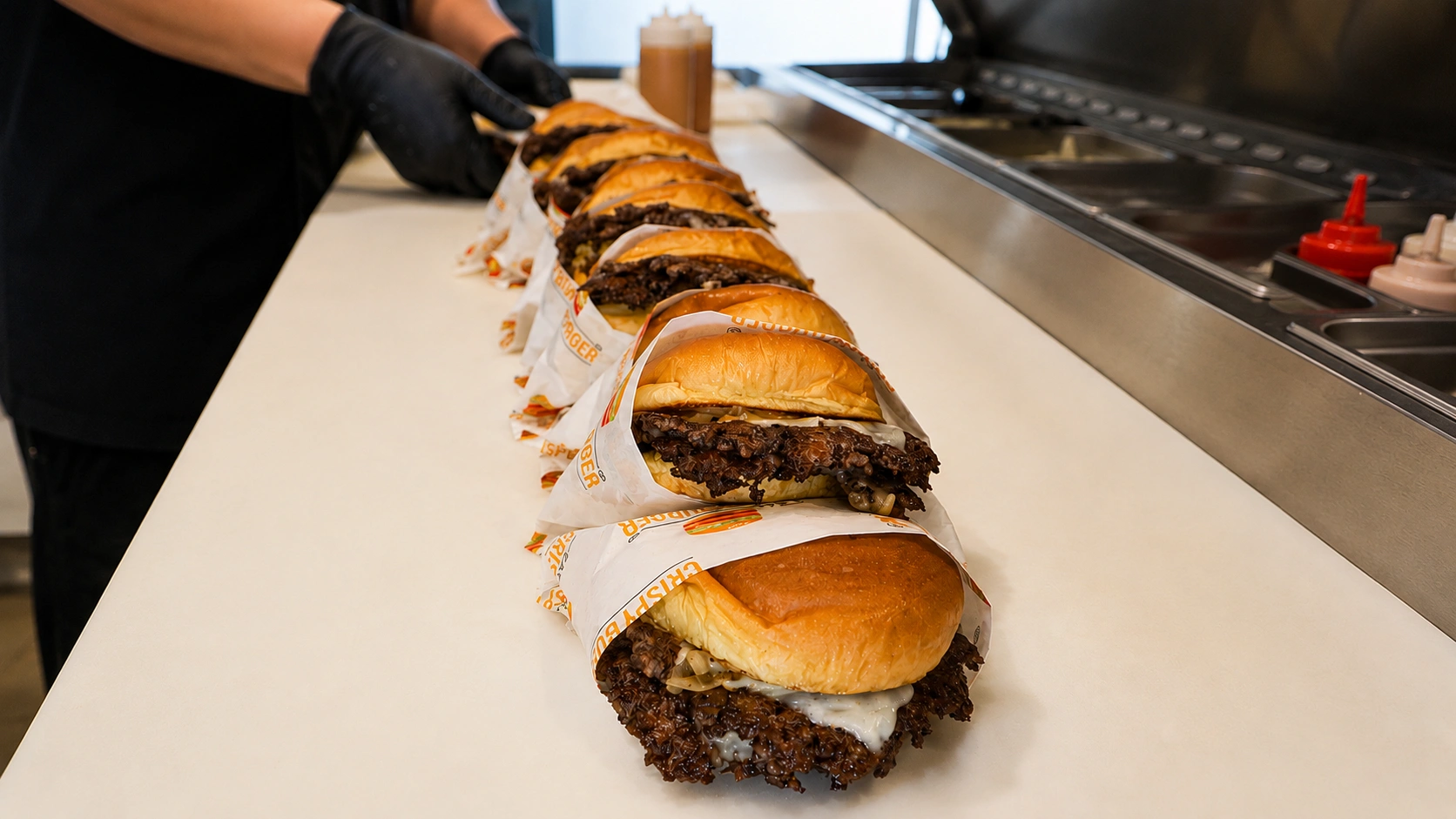 Row of freshly prepared crispy burgers lined up on branded wrapping paper during food preparation.