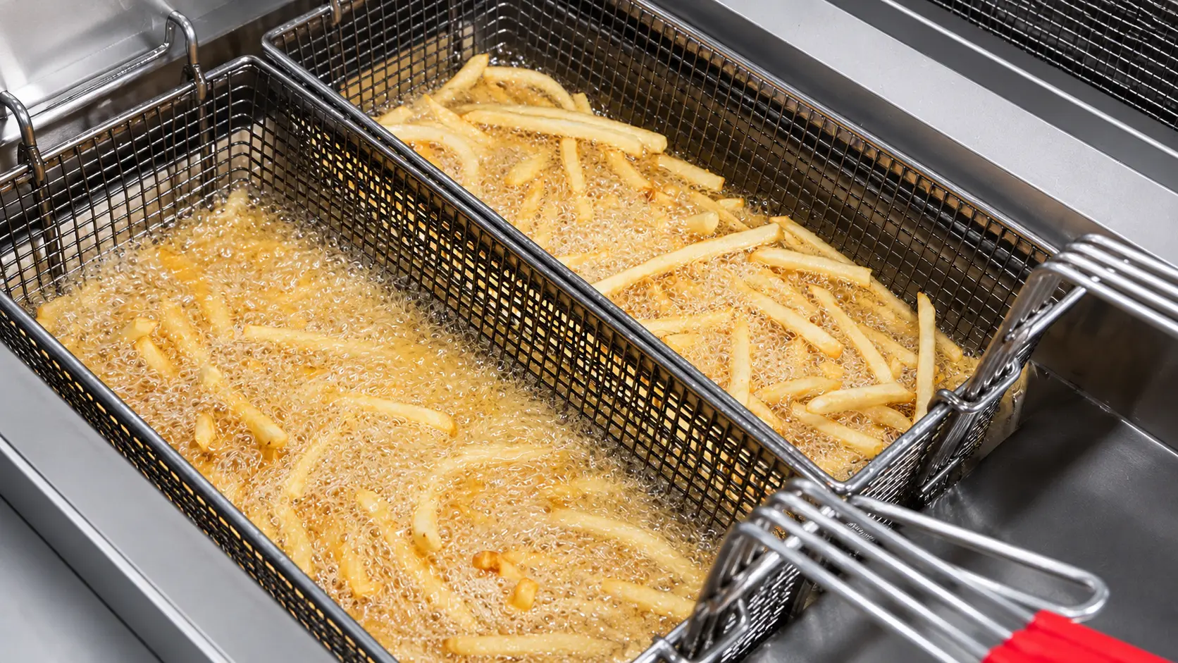 Golden French fries cooking in a deep fryer basket inside a professional restaurant kitchen.